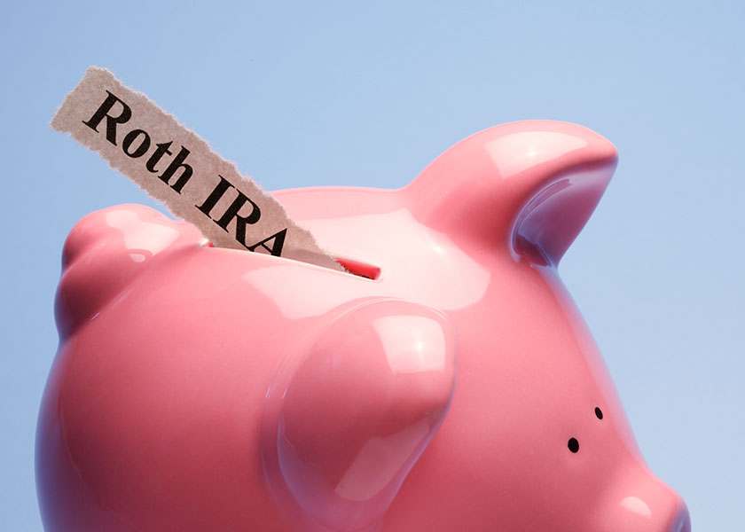 Roth IRA label inserted into a pink piggy bank, symbolizing savings