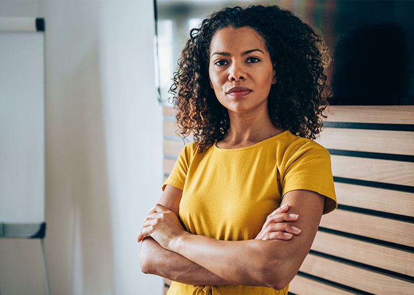 Confident woman in a yellow shirt, standing in a modern office environment. Committed to retirement planning.