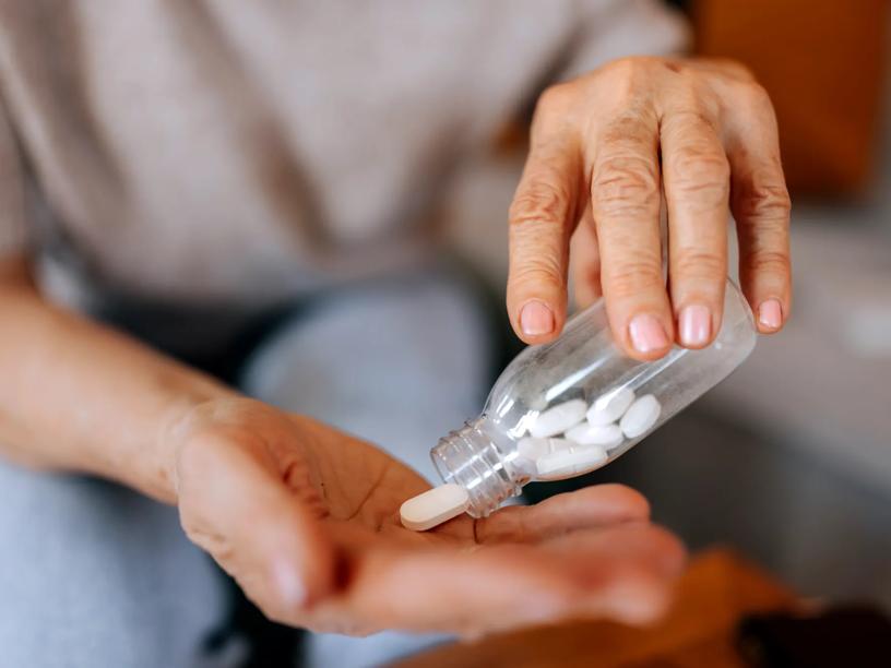 Close-up of an older woman’s hands pouring pills from a bottle.